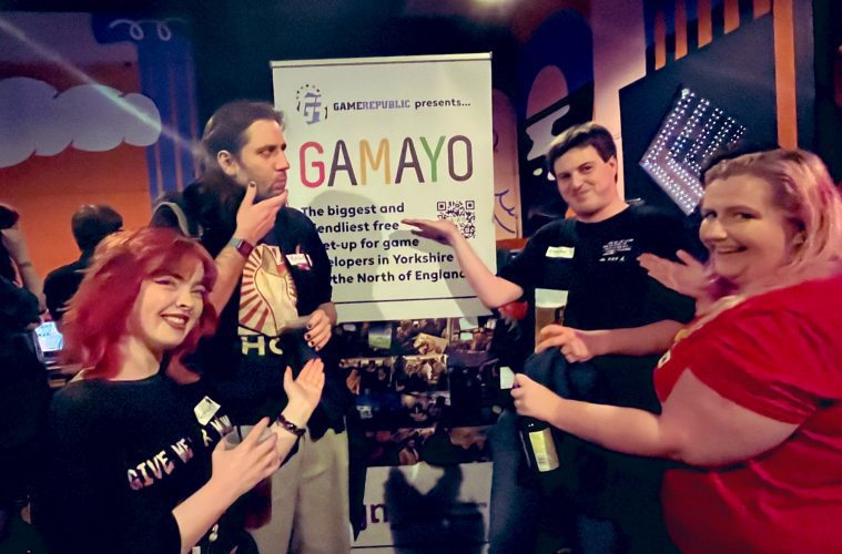GaMaYo attendees stand pointing at a banner saying GaMaYo is the biggest and friendliest game developer network in Yorkshire and The North