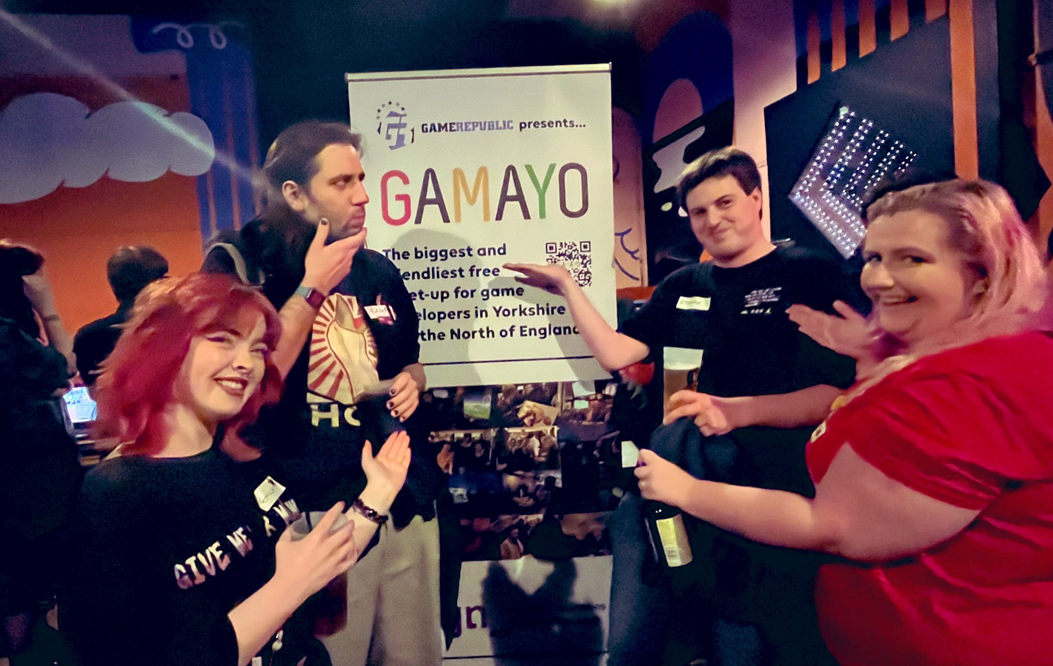GaMaYo attendees stand pointing at a banner saying GaMaYo is the biggest and friendliest game developer network in Yorkshire and The North